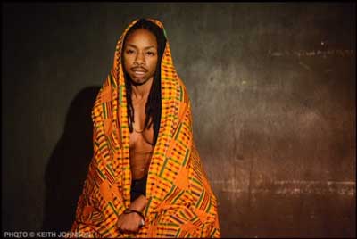 Seattle Drag King D Dynasty poses with an orange, patterned shawl or blanket over their head. Photo by Keith Johnson.