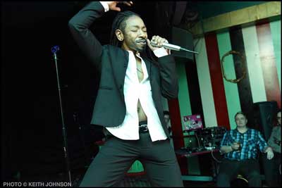 Drag King D Dynasty pictured lip-syncing into a microphone. Photo by Keith Johnson.
